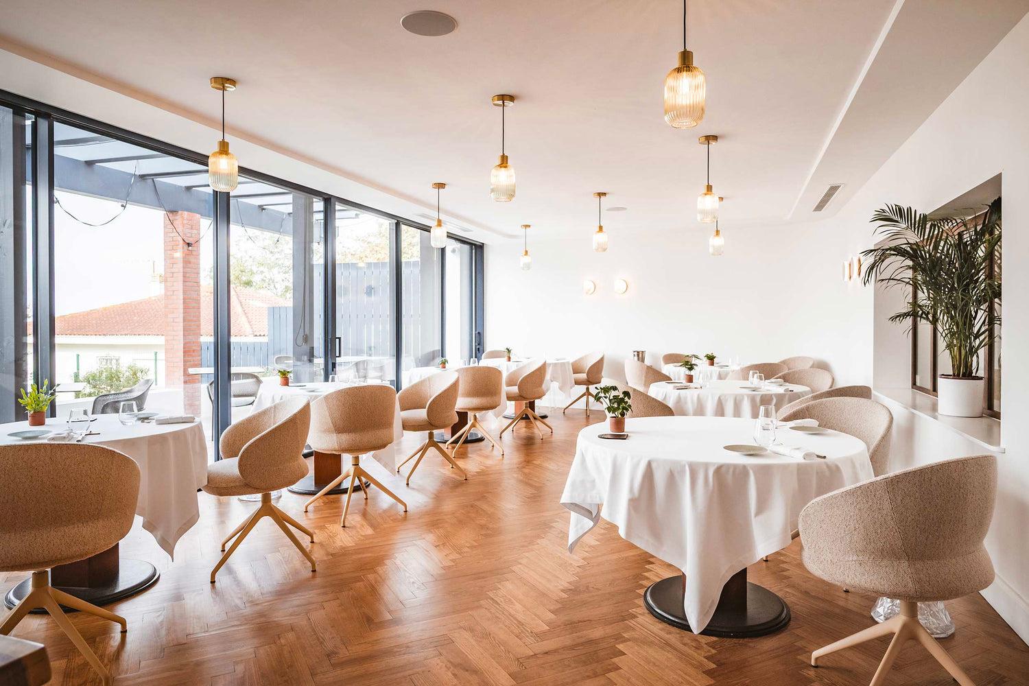 Salle de restaurant lumineuse, tables nappées de blanc et parquet en point de Hongrie