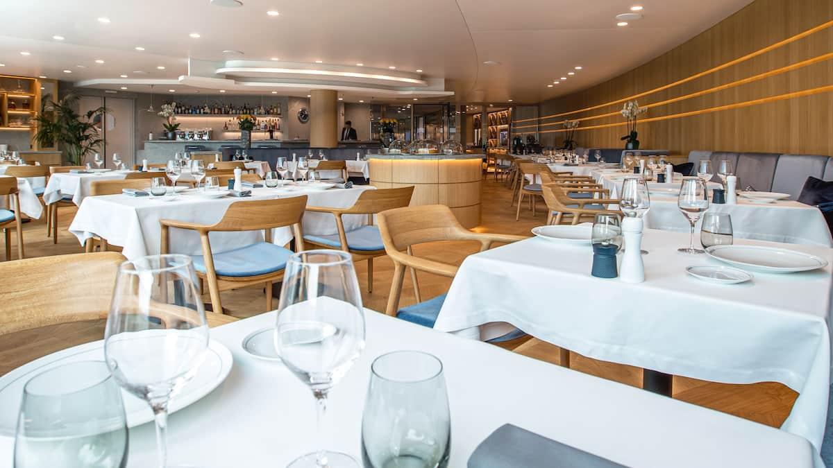 Salle de restaurant dressée, tables nappées de blanc